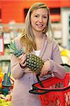 Cheerful young woman holding pineapple with basket in the supermarket