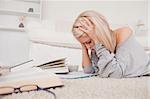 Attractive blond woman frustrated with her books lying on a carpet in the living room