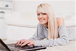 Pretty blond woman relaxing on laptop lying on a carpet in the living room