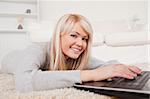 Beautiful blond woman relaxing on laptop lying on a carpet in the living room