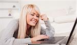 Attractive relaxed woman relaxing on laptop lying on a carpet in the living room