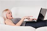 Surprised woman relaxing on laptop lying on a sofa in a studio