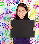 Young Cheerful Girl With A Blank Board And Wall With Colored Hands In The Background