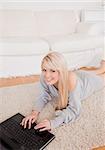 Beautiful young blond woman relaxing on laptop lying on a carpet in the living room