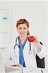 Cute female doctor showing a red apple to the camera in her surgery