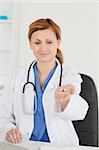 Cute female doctor showing pills to the camera while sitting in her office