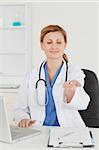 Attractive female doctor showing pills to the camera while sitting in her office