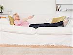 Pretty blonde woman watching tv while lying on a sofa in the living room