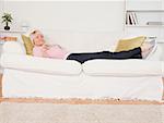 Pretty blonde female watching tv while lying on a sofa in the living room