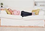 Attractive blonde woman watching tv while lying on a sofa in the living room
