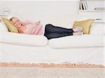 Attractive blonde female watching tv while lying on a sofa in the living room