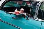 tray with burger and milk shake on classic car at drive in