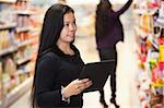Young woman looking at the products while using digital tablet in shopping centre with person in the background