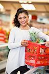 Smiling woman holding basket filled with fruits in supermarket and looking at camera