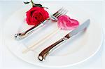 Valentines day table setting with a white plate, single pink rose and heart shaped lolly