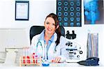 Smiling medical doctor woman sitting at table in office