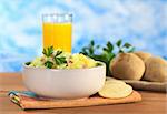 Potato salad made of cooked potatoes, red onions and cucumber, seasoned with a mayonnaise dressing and garnished with a parsley leaf with crackers on the side and orange juice in the back (Selective Focus, Focus on the front of the salad and the leaf)