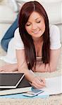 Charming red-haired female studying for while lying on a carpet in the living room