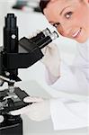 Charming red-haired scientist looking through a microscope in a lab