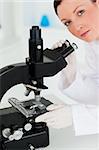 Cute red-haired scientist looking through a microscope in a lab