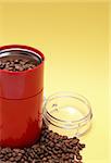 Lot of coffee beans near open modern red grinder on yellow background