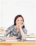 Beautiful joyful red-haired girl studying for an examination at her desk