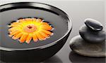 Orange flower floating on a black bowl and a stack of black pebbles