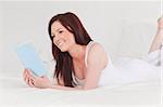 Gorgeous red-haired woman reading a book while lying on her bed