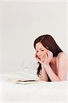 Pretty red-haired woman reading a book while lying on her bed