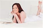 Attractive red-haired woman reading a book while lying on her bed