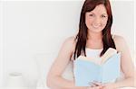Gorgeous red-haired female reading a book while sitting on her bed