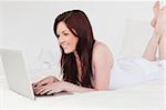 Attractive red-haired female relaxing with her laptop while lying on her bed