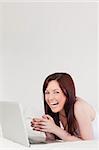 Good looking red-haired female relaxing with her laptop while lying on her bed