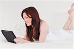 Attractive red-haired female relaxing with her tablet while lying on her bed