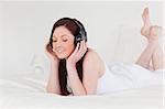 Good looking red-haired female relaxing with her headphones while lying on her bed