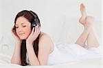 Pretty red-haired female relaxing with her headphones while lying on her bed