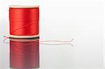 Red spool of thread on a table against a white background