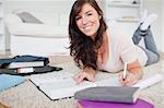 Young gorgeous woman writing on a notebook while lying on a carpet in the living room