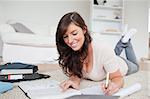 Young cute woman writing on a notebook while lying on a carpet in the living room