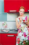 young beautiful woman wearing white and pink dress with cup of morning coffee in interior of red modern kitchen