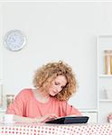 Charming blonde woman relaxing with her tablet while sitting in the kitchen in her appartment