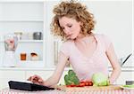 Pretty blonde woman relaxing with her tablet while cooking some vegetables in the kitchen in her appartment