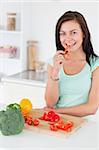 Cute brunette eating a slice of pepper while looking at the camera