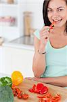 Portrait of a cute brunette eating a slice of pepper while looking at the camera