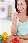 Portrait of a smiling brunette eating a slice of pepper while looking at the camera