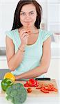 Portrait of a charming woman eating a slice of pepper while looking at the camera