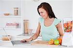 Woman with a laptop and fruits in a blender in her kitchen