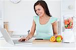 Young brunette with a laptop and fruits in her kitchen