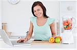 Cute brunette with a laptop and fruits in her kitchen