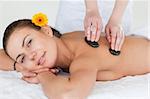 Close up of a cute brunette enjoying a hot stone massage with a flower on her ear